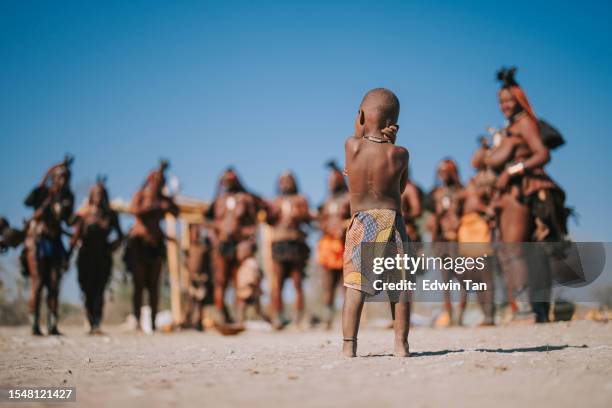 rückansicht namibianisches himba-kind, das dorfbewohner anschaut - himba stock-fotos und bilder