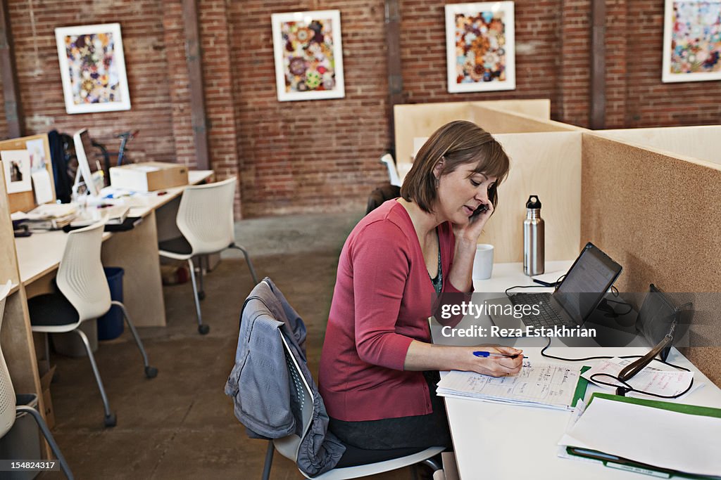 Woman listens on cell phone as she makes notes