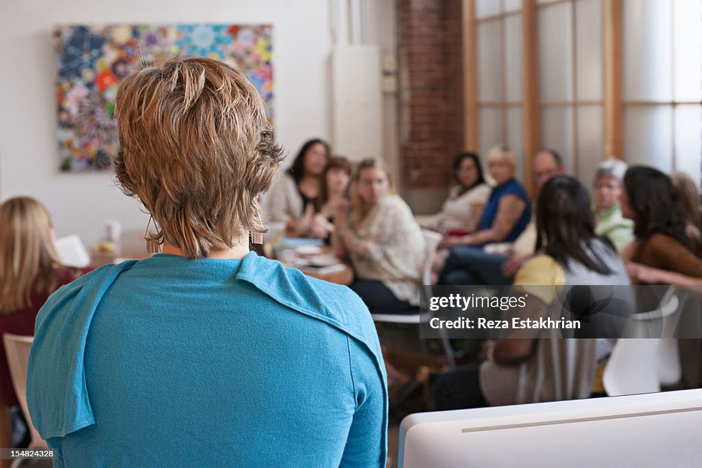 Woman stands at back of business meeting