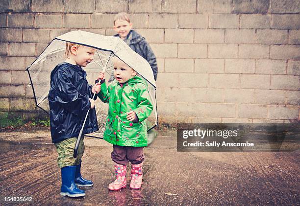 two children sharing an umbrella in the rain - child umbrella stockfoto's en -beelden