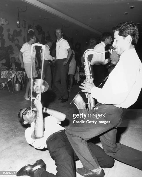Trombonist plays while leaning backwards on the ground with a saxophonist performing over him as people dance inside a 'Cazino' nightclub in Mamaia,...