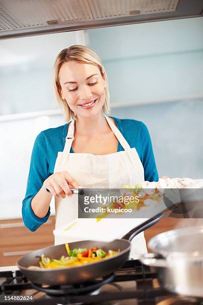 junge frau steht auf einen gas stove kochen gesunde speisen - köchin stock-fotos und bilder