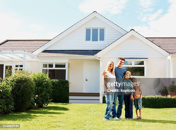 caucasian family standing in front of a luxury house - family of four in front of house stock pictures, royalty-free photos & images