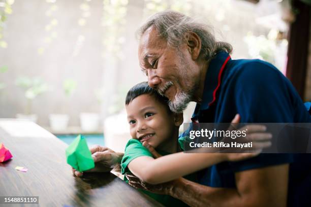 nettes asiatisches enkelkind, das seinen großvater umarmt. - kids fun indonesia stock-fotos und bilder