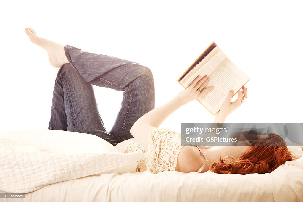 Redhead woman lying in bed reading a book