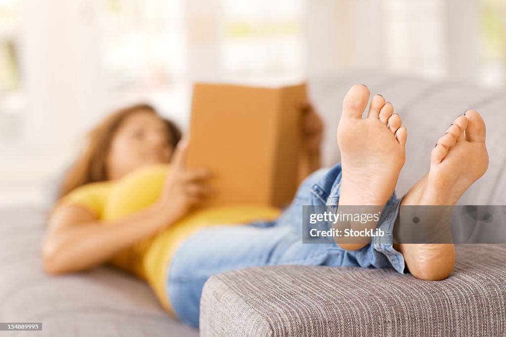 Young woman lying on sofa at home, reading