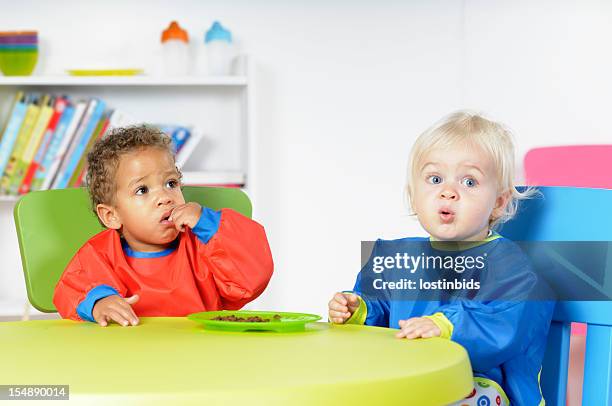 babies/ toddlers  at mealtime in a nursey setting - bib stock pictures, royalty-free photos & images
