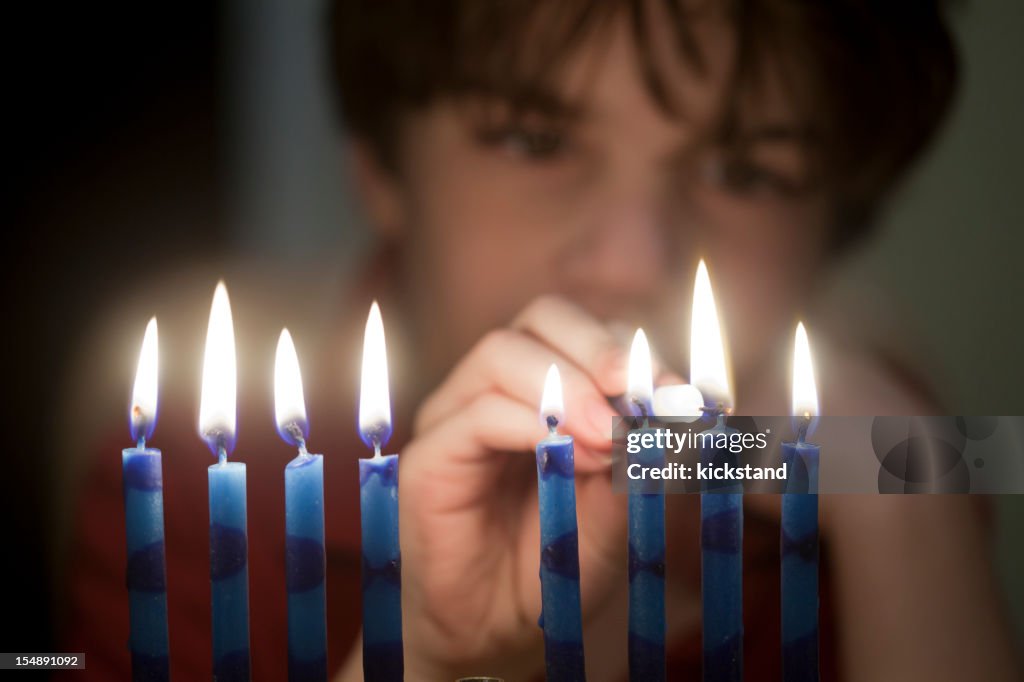 Out-of-focus boy lighting up a menorah in first plane