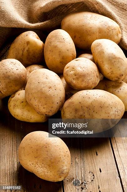 raw kartoffeln aus einem sack auf rustikalen holz-tisch - potatoes in a sack stock-fotos und bilder