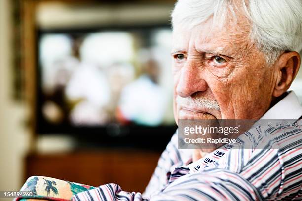 grumpy old man looks round from television, frowning - lentigo stockfoto's en -beelden