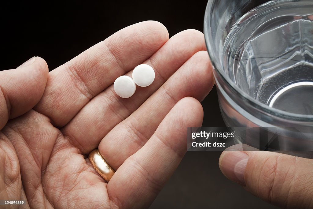 Hands holding two aspirin and a glass of water