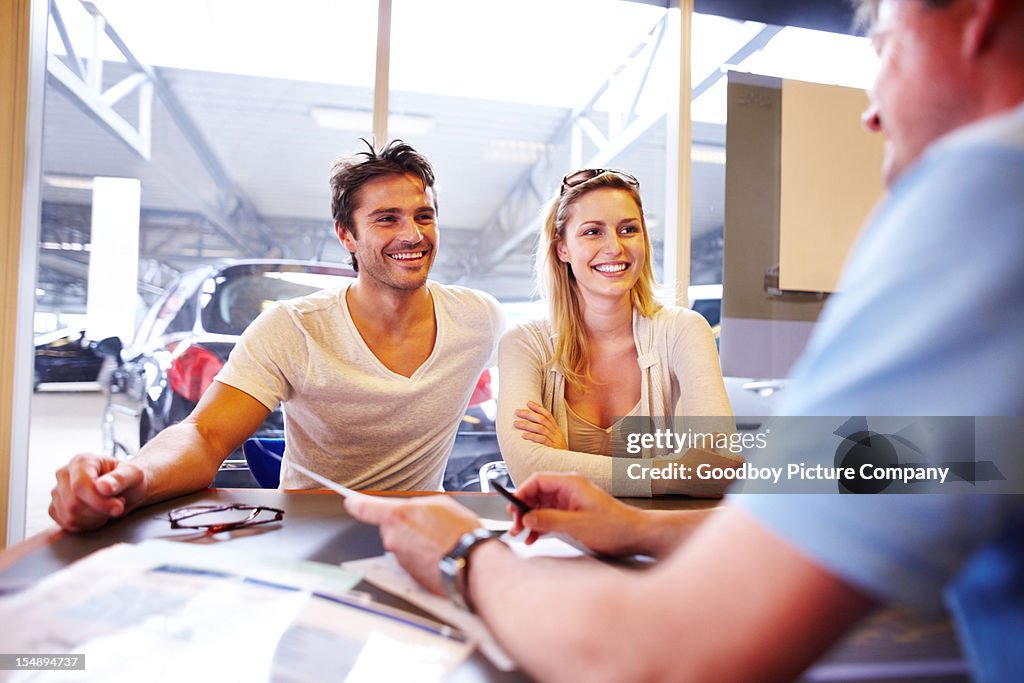 Attractive young couple in automobile showroom buying a new car