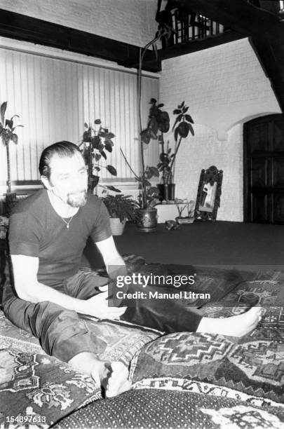 Maurice BEJART sitting on cushions in his apartment in Brussels, Around his neck, he wears a mini-Koran has suspended a thin gold chain.