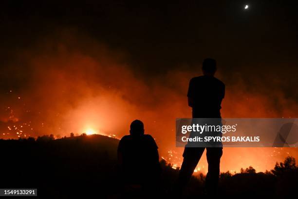 People watch the fires near the village of Malona in the Greek island of Rhodes on July 23, 2023. Tens of thousands of people fled wildfires on the...