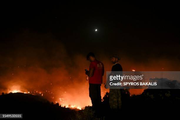 People watch the fires near the village of Malona in the Greek island of Rhodes on July 23, 2023. Tens of thousands of people fled wildfires on the...