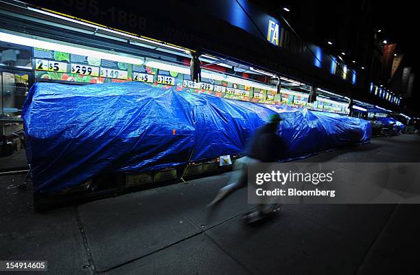 Pedestrian rides past fruit and vegetable stalls covered with tarps on Broadway in New York, U.S., on Sunday, Oct. 28, 2012. The U.S. Securities...