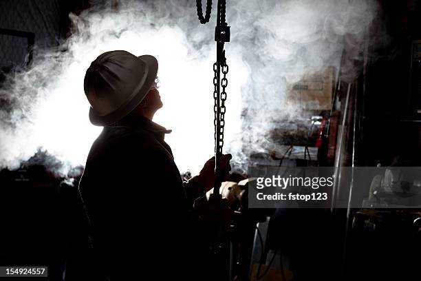 silhouette of man using chain hoist in workshop. - oliewerker stockfoto's en -beelden