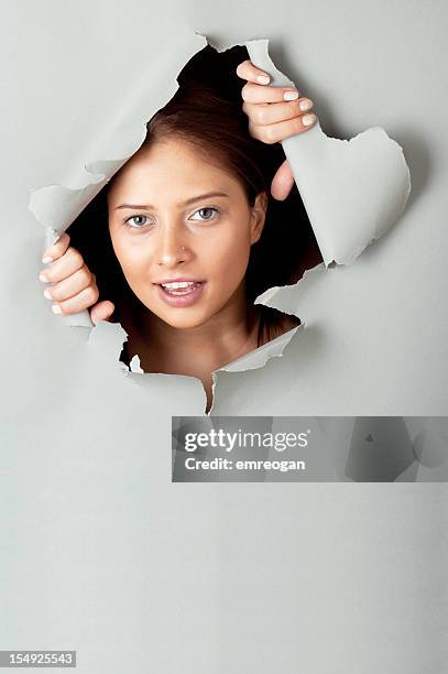 young woman looking out through hole in grey paper - peeping holes stock pictures, royalty-free photos & images