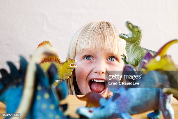loura engraçada criança pequena roars no seu ferocious dinosaurs de brinquedo - dinossauro imagens e fotografias de stock