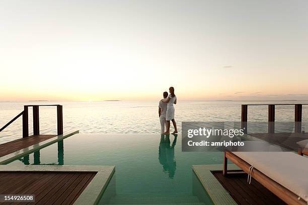 couple admirant le coucher du soleil au bord de la piscine - premium photos et images de collection