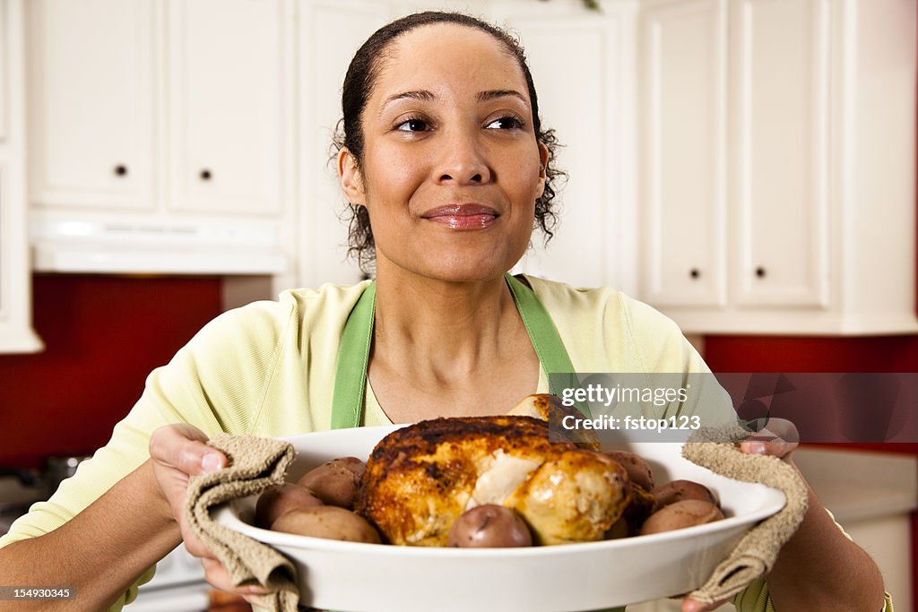 Woman in kitchen enjoying aroma of baked chicken dish.