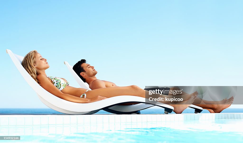 Relaxed couple sunbathing by swimming pool