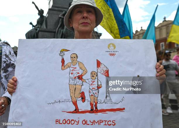 Protester in Krakow holds a powerful poster with Putin and Lukashenko's images, featuring an Olympic torch covered in blood and the words 'Bloody...