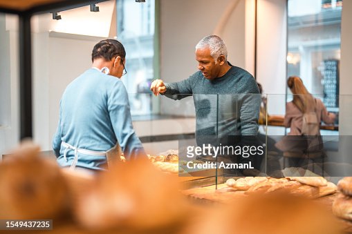 Mature Hispanic Male Selecting Fresh Bread At An Artisan Bakery