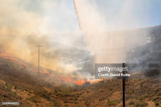 Water falls from a bucket carried by a helicopter as fire crews battle a new fire that started near the Manastash Vista Point along Interstate 82 on...