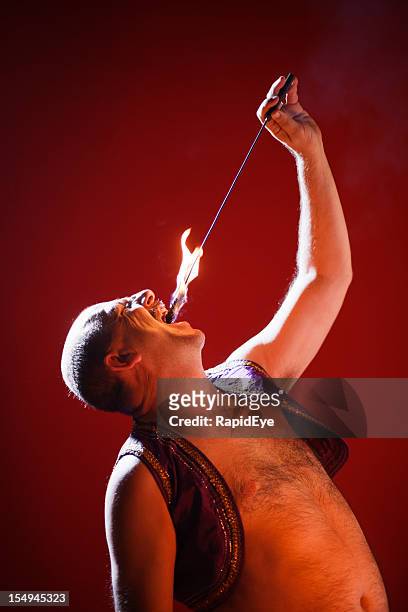 fire eater in action against red background - variety shows stock pictures, royalty-free photos & images