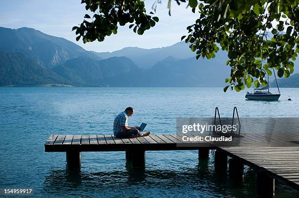 man with laptop sitting on a jetty - bergsteiger stockfoto's en -beelden