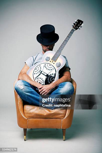 mann mit gitarre sitzt auf sessel - dobro stock-fotos und bilder