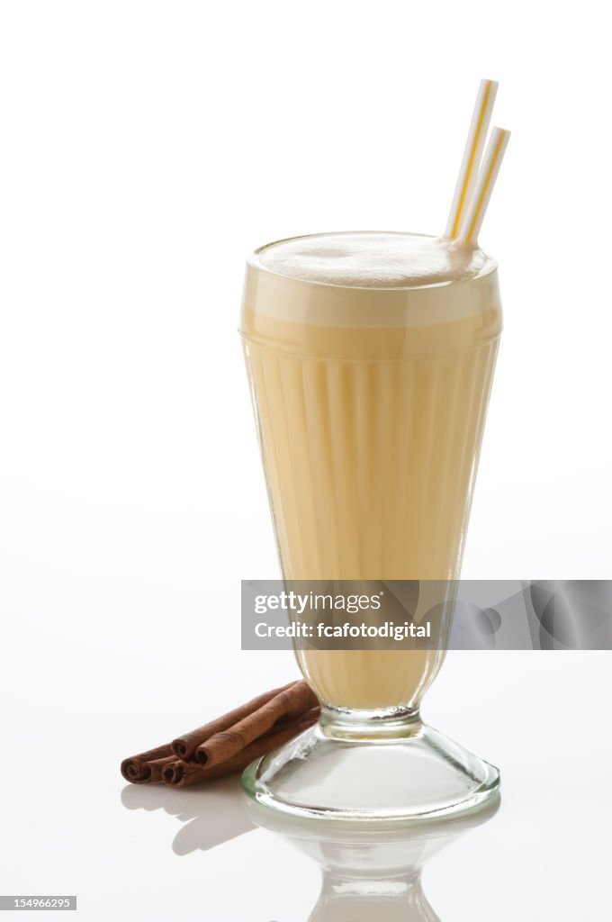 Classic glass of vanilla milkshake on white backdrop.