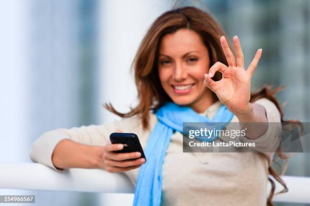30 代の女性を持つ携帯電話およびギブ ok の標識 - okサイン　女性 ストックフォトと画像