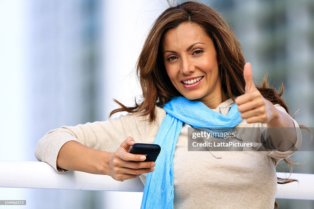 Young female holding cell phone and gesturing thumbs up