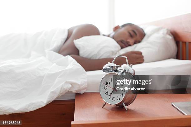 rádio relógio na mesa de cabeceira - black man sleeping in bed - fotografias e filmes do acervo