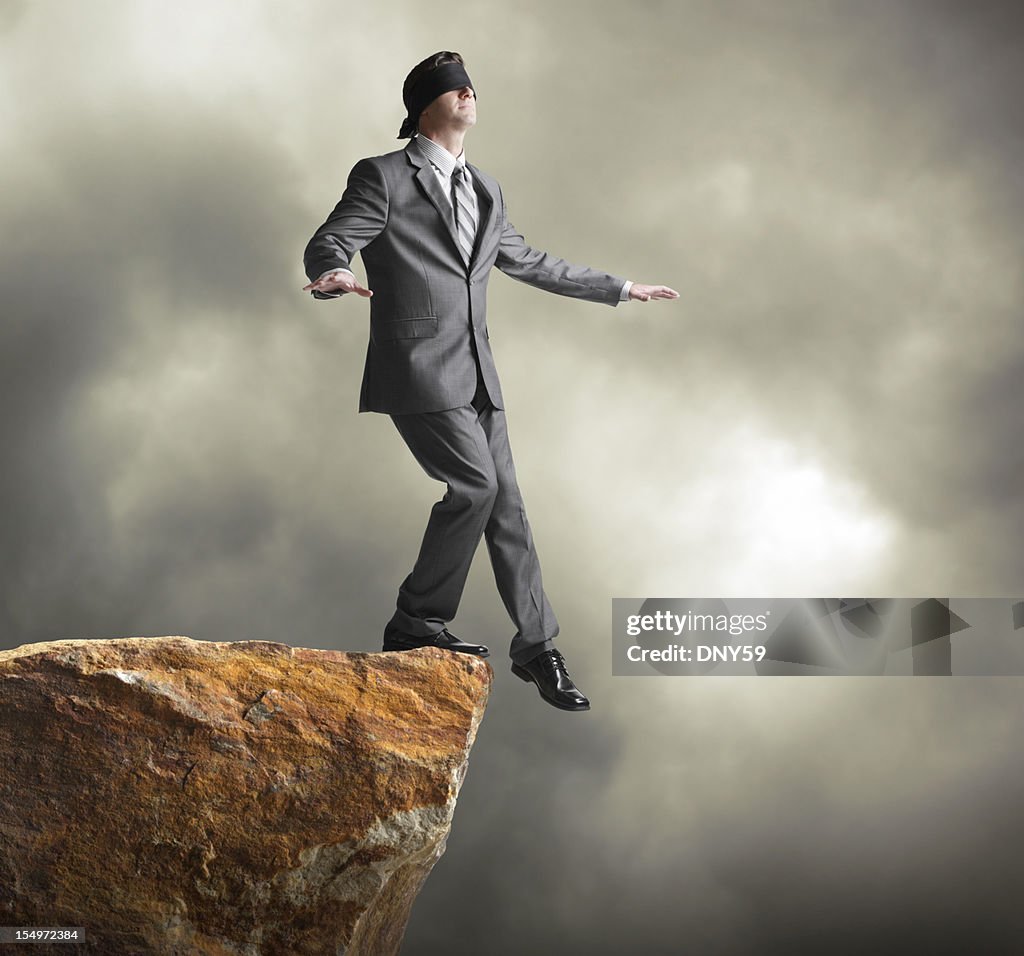 Blindfolded businessman about to step off of a cliff