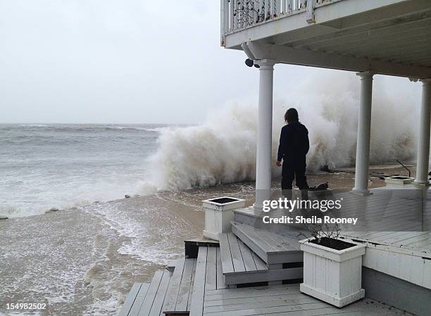 Wave crashes against the shore while person stands on a porch as Hurricane Sandy moves up the coast October 29, 2012 in Montauk, New York. Sandy,...