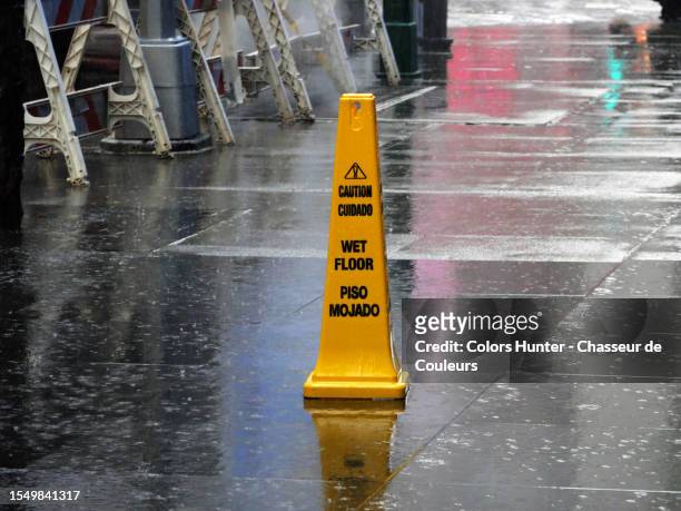 " caution wet floor - cuidado piso majado " written on a yellow plastic sign placed on a sidewalk during a rain in manhattan, new york state, united states - cuidado stock-fotos und bilder
