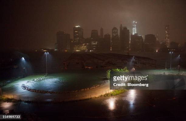 Flood waters cover a promenade in Brooklyn as numerous buildings in Lower Manhattan, background, stand in darkness in New York, U.S., on Monday, Oct....