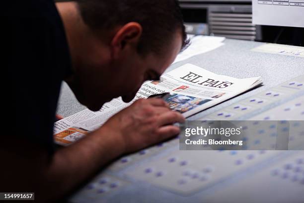 An employee uses a magnifying glass to check the print quality of an El Pais daily newspaper during printing at the El Pais printing plant in Madrid,...