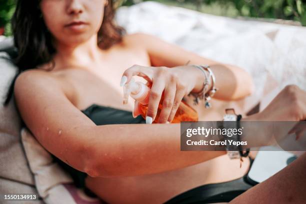 a woman spritzes her arm with spray sun screen at pool - bronzeado imagens e fotografias de stock
