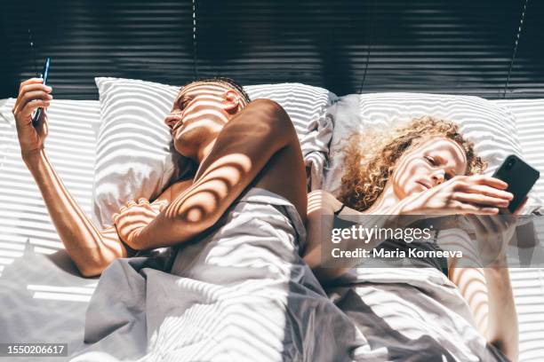 young couple lying in bed and using a smartphone at home. - heure du coucher photos et images de collection