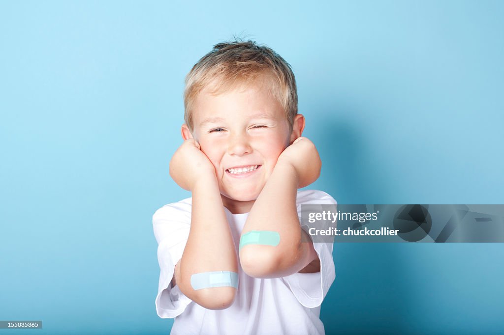 Young boy happily showing of the bandages on his elbows