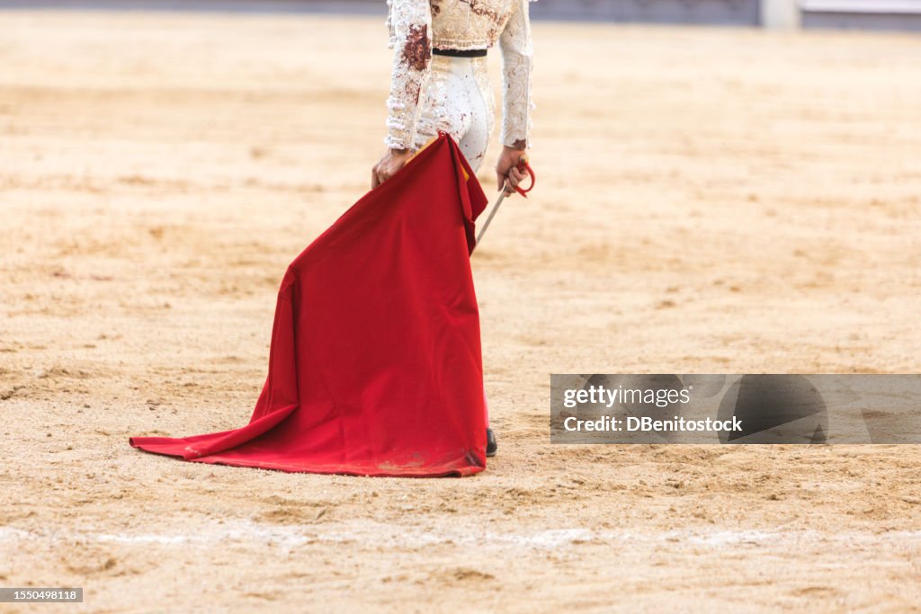 Unidentified bullfighter wearing bloodstained silver bullfighter suit, holding crutch and rapier, in arena. Bullfighting, corrida, fiesta, tradition and bullfighter concept.
