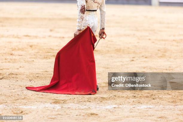 unidentified bullfighter wearing bloodstained silver bullfighter suit, holding crutch and rapier, in arena. bullfighting, corrida, fiesta, tradition and bullfighter concept. - bullfighter stock pictures, royalty-free photos & images