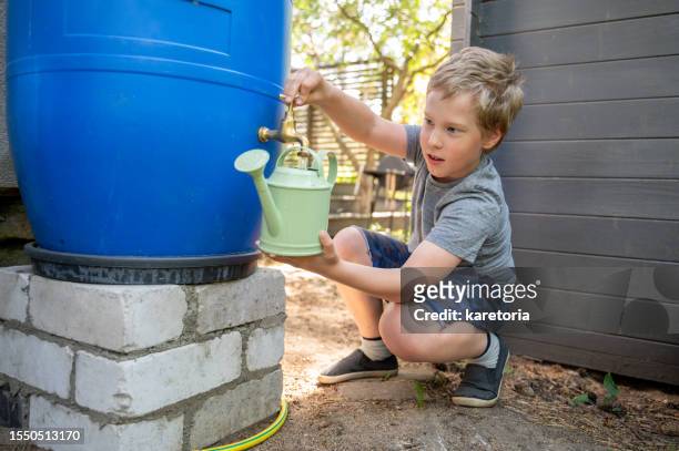 boy filling watering can with water - rainwater tank stock pictures, royalty-free photos & images
