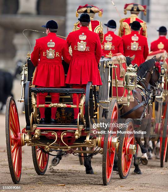 Two of Queen Elizabeth II's Royal Coachmen wearing red and gold livery with the ER cypher stand on the rear of the open carriages taking part in the...