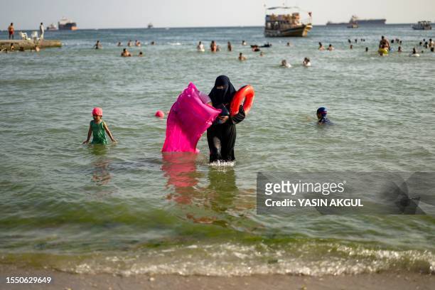 Woman wearing a hijab holds a lilo and rubber ring as she exists the sea at Menekse beach in Istanbul on July 23, 2023. Turkey is bracing for an...