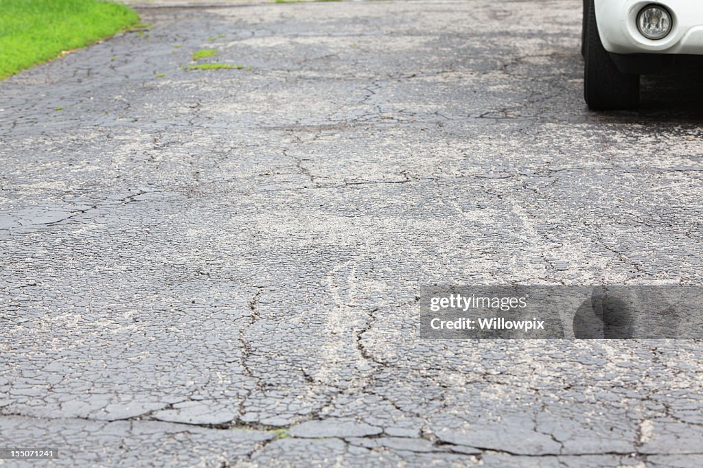 Cracked asphalt driveway with car parked